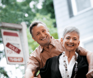 Couple smiling in front of home sale sign