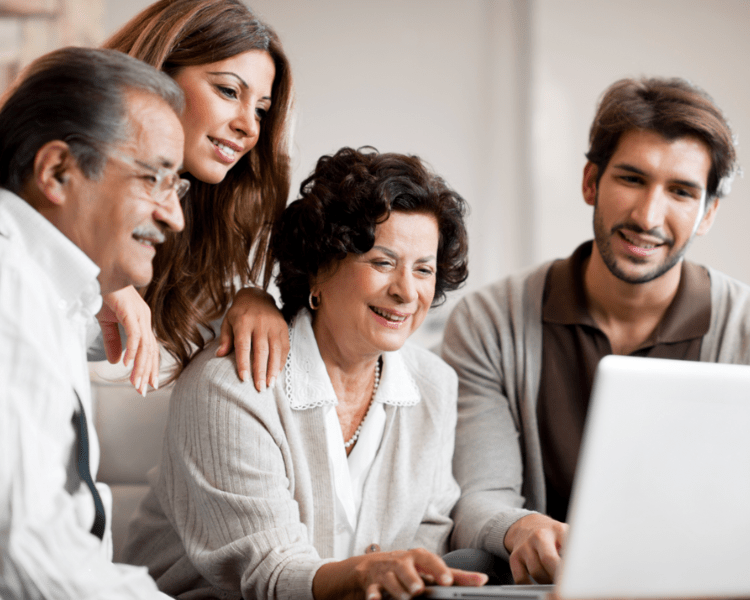 Four adults gathered around a laptop, smiling as they look at the screen.